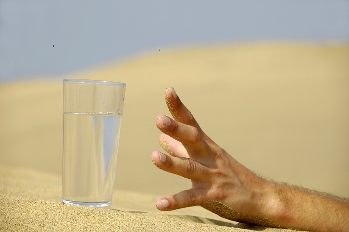 A hand reaching for a glass of water in the desert dehydration